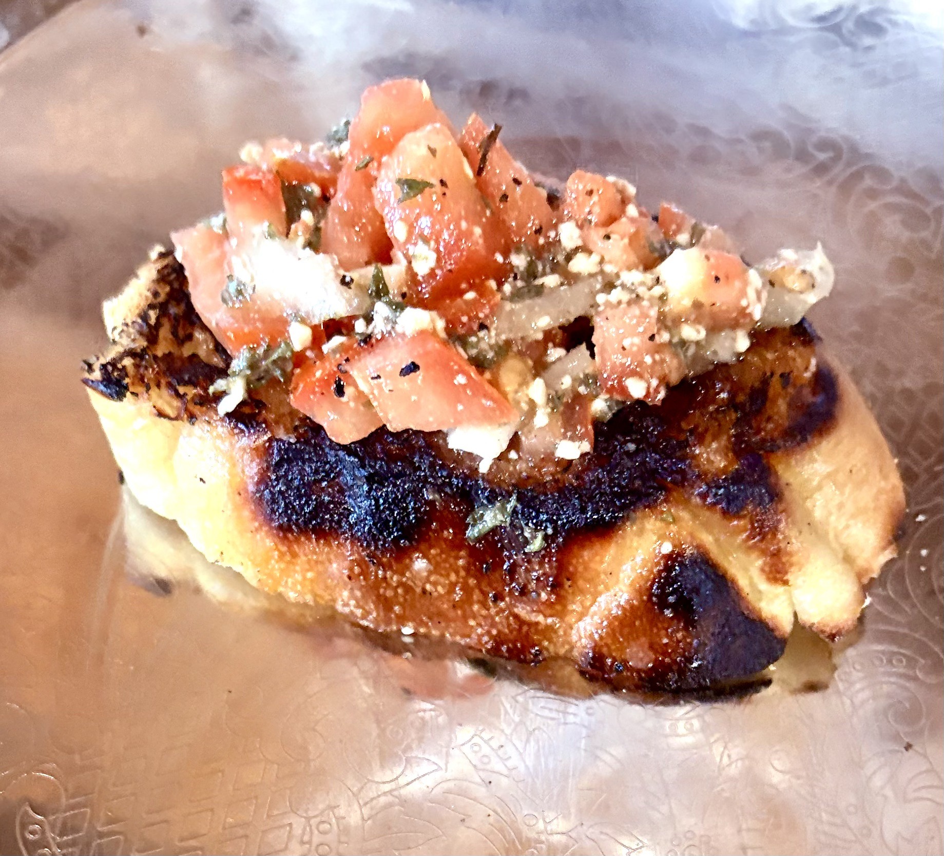 Grilled bread topped with fresh tomato and onion salsa, served on an ornate plate, highlighting a delicious appetizer.