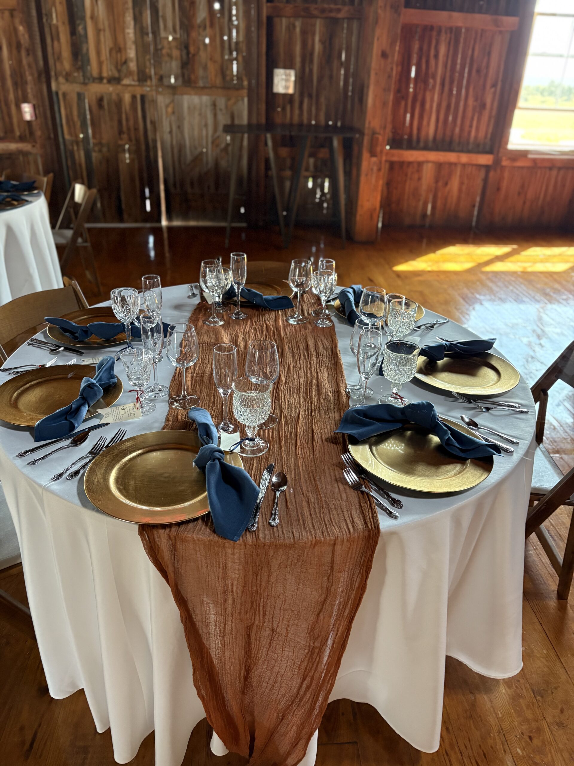Elegant dining setup featuring a table with gold chargers, blue napkins, and crystal glassware, set against a rustic wooden backdrop.