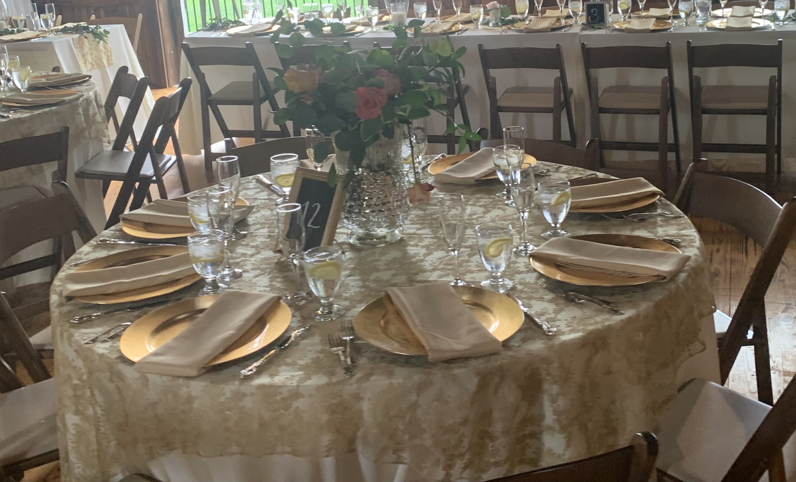 Elegant dining setup for an event, featuring a gold and cream tablecloth, beautiful floral centerpiece, and place settings with gold plates and crystal glassware.