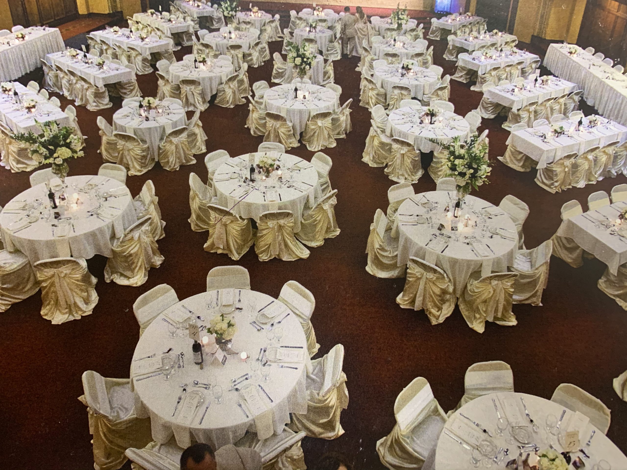 Elegant banquet hall with multiple round tables, each dressed in white and gold, adorned with floral centerpieces, ready for an event.